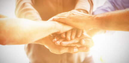 Image of a group of individuals placing their hands together in an inner circle as if to represent teamwork.